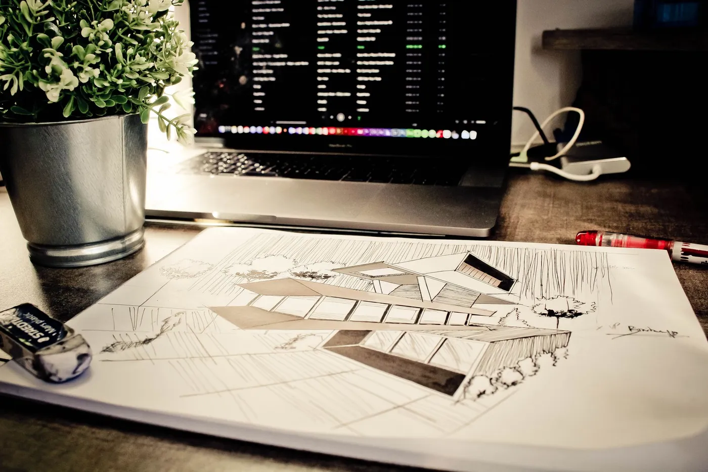 Mimari eskiz, dizüstü bilgisayar ve yeşil bitkinin bulunduğu çalışma masası